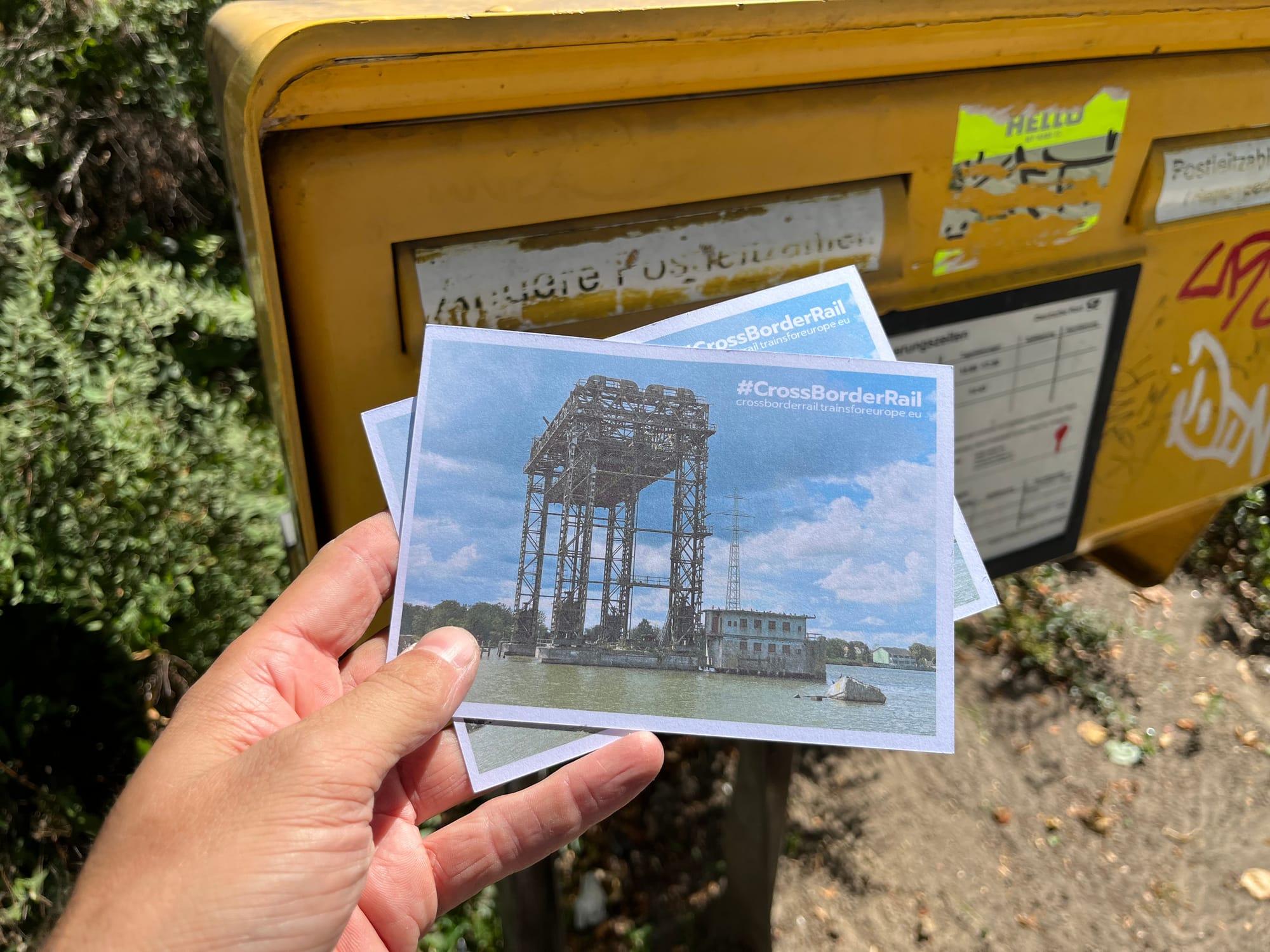 Jon holding two postcards in front of a German postbox